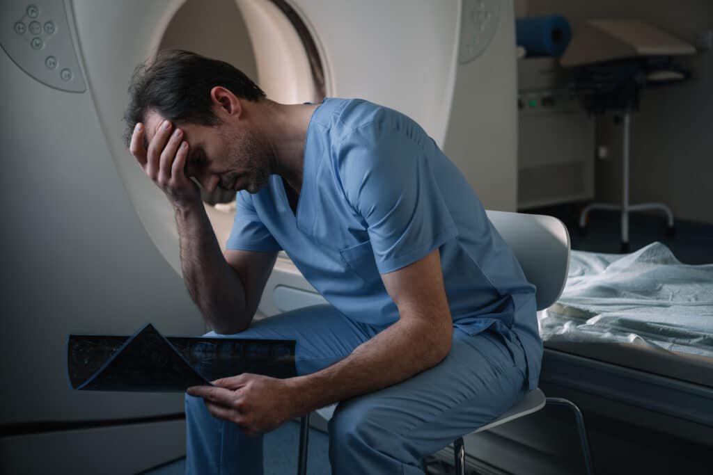 exhausted sitting near computed tomography scanner in hospital and holding x-ray diagnosis